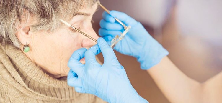 An ophthalmologist in blue gloves takes off his glasses from an elderly 80 female patient, a pensioner, due to improved vision after pupil surgery. Professional optics, medicine and healthcare