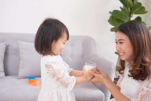 Little girl and her mom drinking milk sitting on sofa at home. Motherhood and care, healthy eating and lifestyle, early development concept, copy space