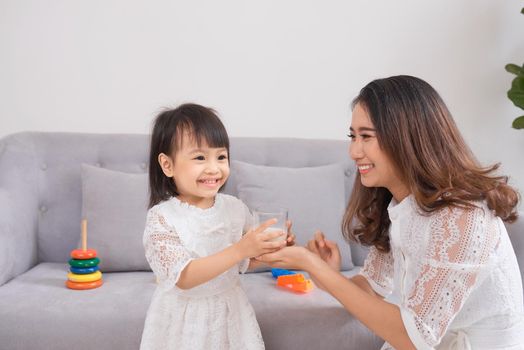 Little girl and her mom drinking milk sitting on sofa at home. Motherhood and care, healthy eating and lifestyle, early development concept, copy space