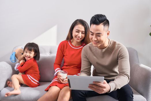 family, technology, parenthood and people concept - happy mother and father showing tablet pc computer to little daughter at home