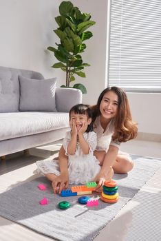 Happy loving family. Mother and daughter are doing play a toy and having fun. Mother and daughter doing your education sitting on the floor in the living room.