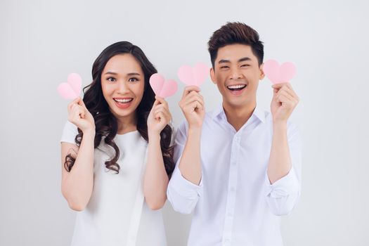 Happy young Vietnamese couple is holding pink paper hearts and smiling