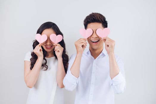 Happy young Vietnamese couple is holding pink paper hearts and smiling