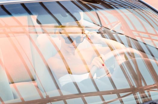 Young trendy woman driving modern car looking above sunglasses