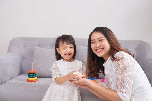 Little girl and her mom drinking milk sitting on sofa at home. Motherhood and care, healthy eating and lifestyle, early development concept, copy space