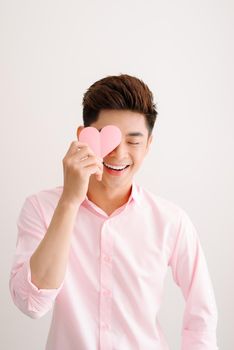 Handsome asian man holding pink heart paper posing on gray background