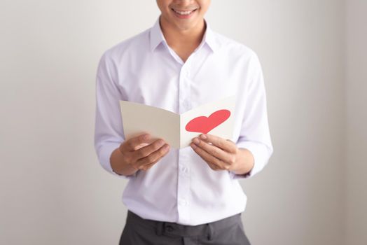 Young handsome asian man reads greeting card with heart shape on white background