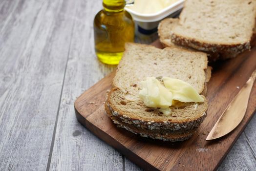 slice of butter and whole meal bread on chopping board .