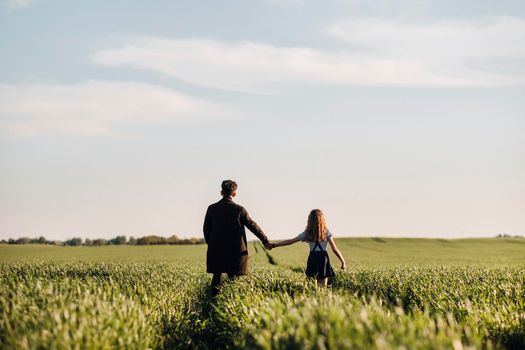 teenage daughter walks with her father in a meadow holding hands in the evening.