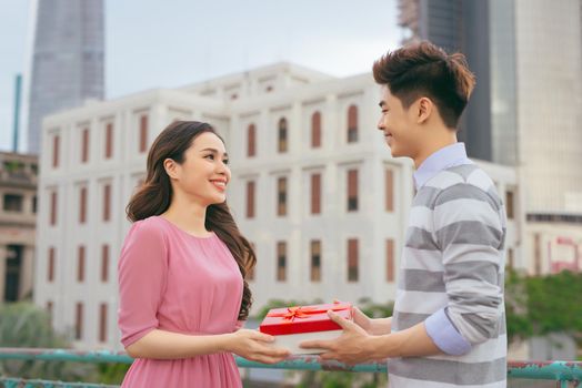 Man giving to his woman a gift. Asian couple in love outdoors 