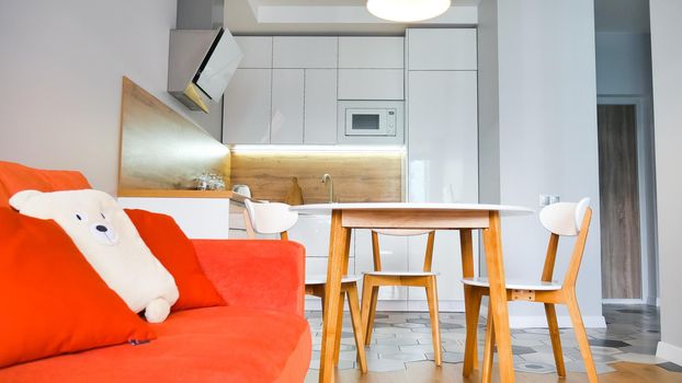 Modern kitchen interior with wooden and white elements, bright orange sofa, domestic life, home showcase interior concept