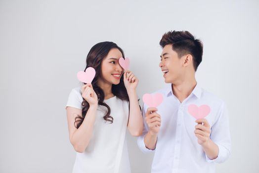 Happy young Vietnamese couple is holding pink paper hearts and smiling