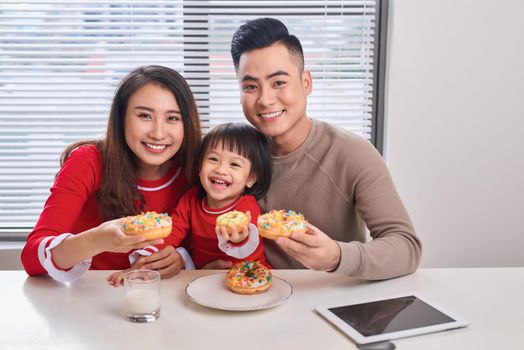 Happy young family with children enjoying breakfast in a white sunny dining room with a big garden view window