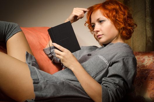 Red woman sitting on sofa reading small black notebook
