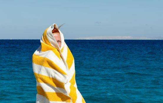 Young woman covers herself with beach towel because of winter wind in Egypt