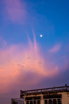 Pink clouds and moon in sunset sky and the old building