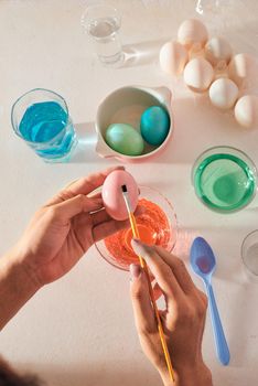 Holidays, tradition and people concept - close up of man hands coloring easter eggs with brush -