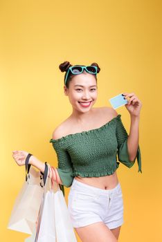 Shopping asian woman holds shopping bags and a credit card on yellow background