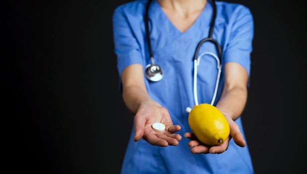 Woman doctor stretches her hands forward, on one hand is lemon fruit, in the other - tablet of vitamin C, an analogue of fruit in the form of tablet, in which a concentrate of vitamins. Fighting colds