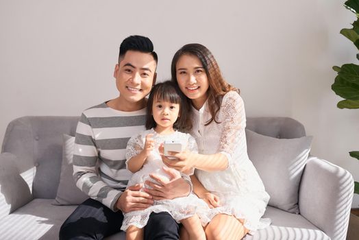 happy parents with cute little daughter sitting on couch and smiling at camera