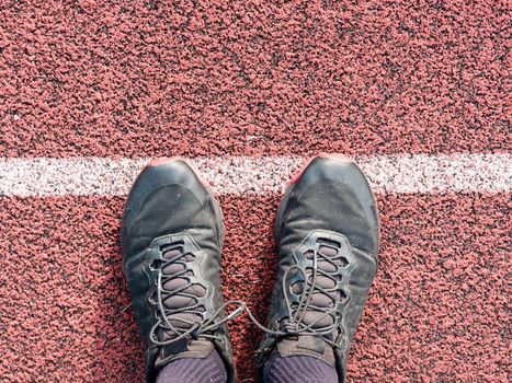 Feet in sneakers stand near the starting line on the red asphalt. Bounding line