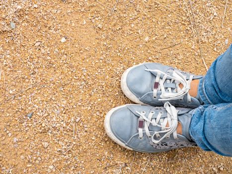 Close-up of girl's legs in denim sneakers and tight slim fit denim pants. Walk through the park on foot.