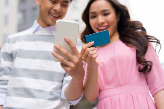 Shoppers buying on line with credit card and smart phone standing beside a storefront on the street