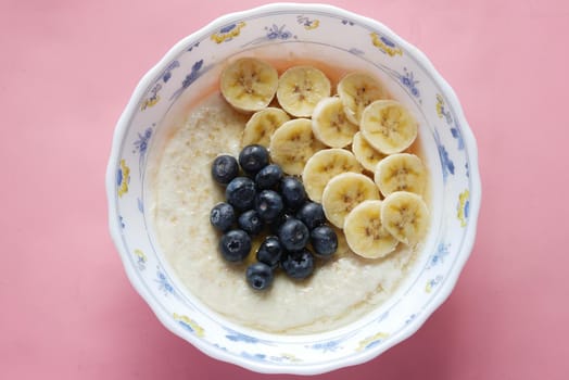 a bowl of oats, berry, banana and honey on pink