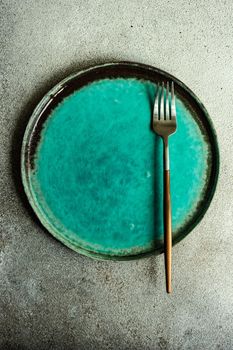Minimalistic place setting with ceramic plate and modern cutlery set on concrete background