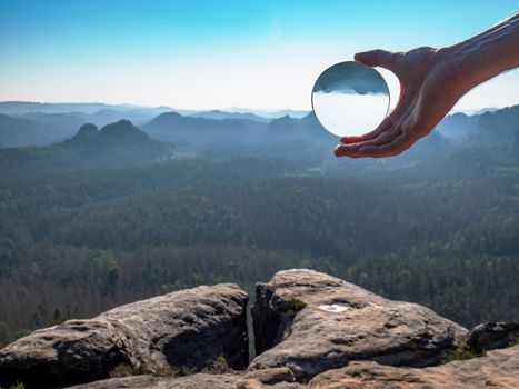 Crystal glass ball in a man's hand. The morning misty hilly landscape is reflected in the lens.