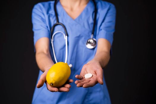 Woman doctor stretches her hands forward, on one hand is lemon fruit, in the other - tablet of vitamin C, an analogue of fruit in the form of tablet, in which a concentrate of vitamins. Fighting colds