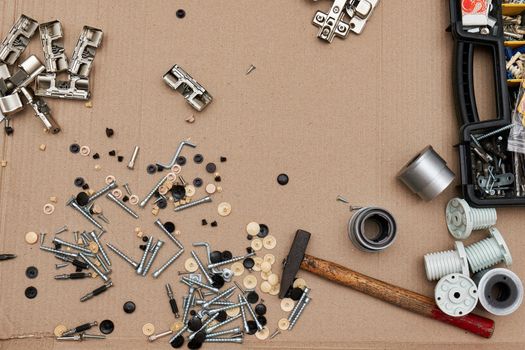 Screws and furniture fittings with a hammer against the background of cardboard from the packaging, the view from above.