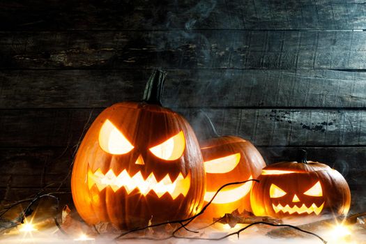 Halloween pumpkins head jack o lantern, candles and dry maple leaves in mist