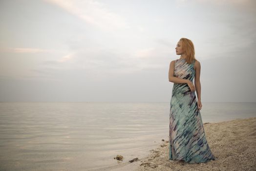 Young red woman wearing long dress on a beach