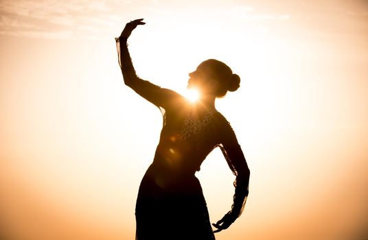 Silhouette of the woman dancing at the beach during beautiful sunrise