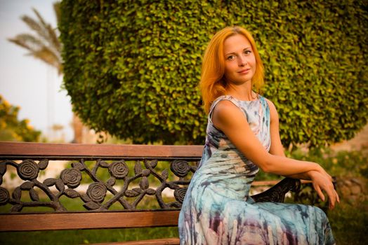 Young red woman wearing long dress sitting on a bench