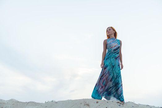 Young red woman wearing long dress on a beach