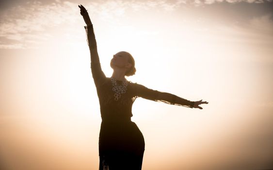 Silhouette of the woman dancing at the beach during beautiful sunrise