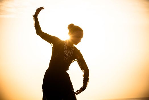 Silhouette of the woman dancing at the beach during beautiful sunrise