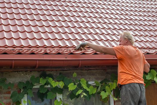 A man cleans out debris and leaves from the gutter system on the roof of his house.