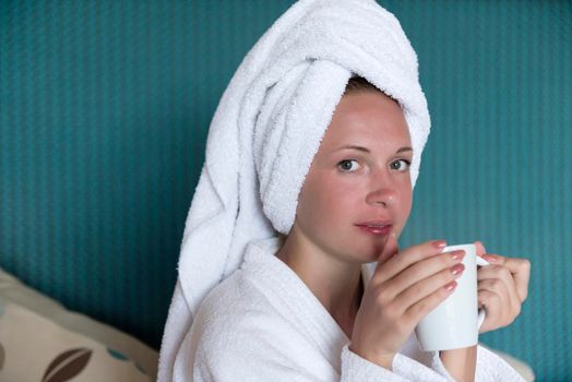 Young woman on the sofa drinking some coffee with shower towel