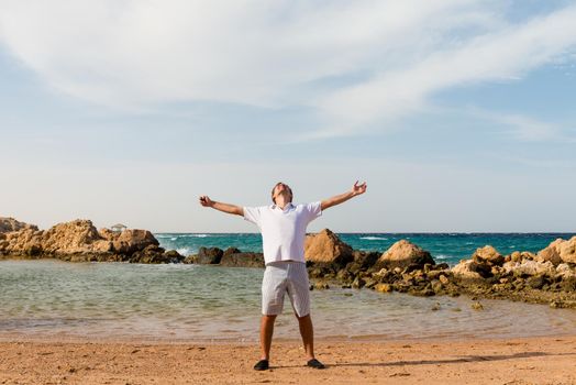 Happy young man with outstretched arms at the beach