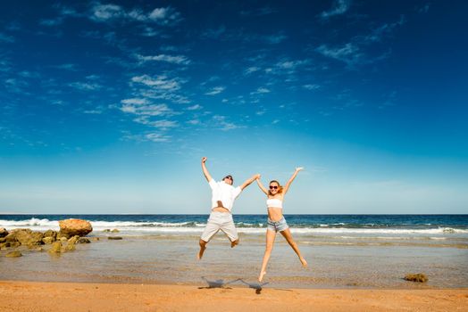 Happy caucasian couple having fun at the beach jumping