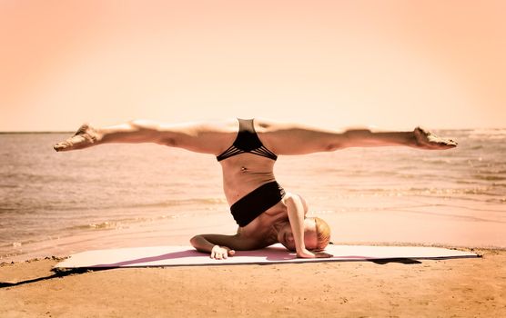 Young woman performing splits while standing on hands and shoulders at the beach
