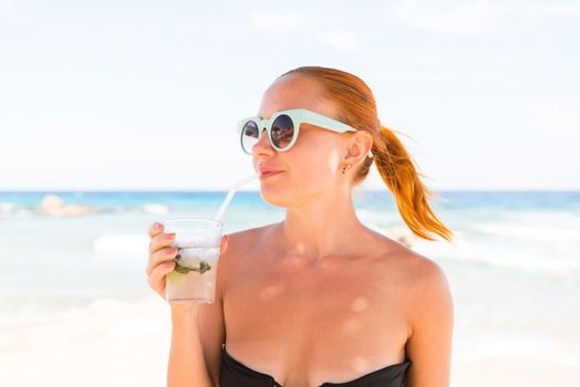 Young woman with glass of mojito wearing bikini at the beach