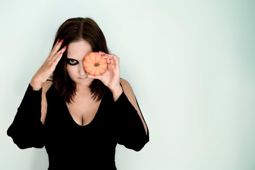 Girl with Halloween makeup on face and pumpkin in hands. Copy space.