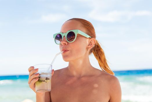 Young woman with glass of mojito wearing bikini at the beach