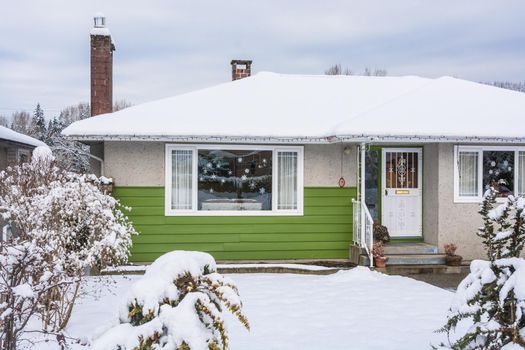 Family house with front yard in snow. Colorful residential house on winter cloudy day