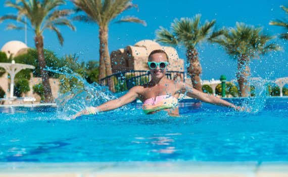 Happy young woman having fun with water splashes in pool