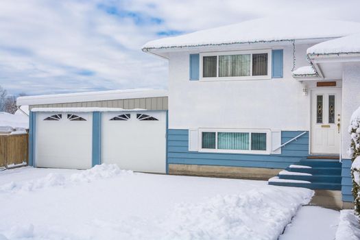 Entrance of residential house with front yard in snow. Beautiful North American house with double garage on winter cloudy day